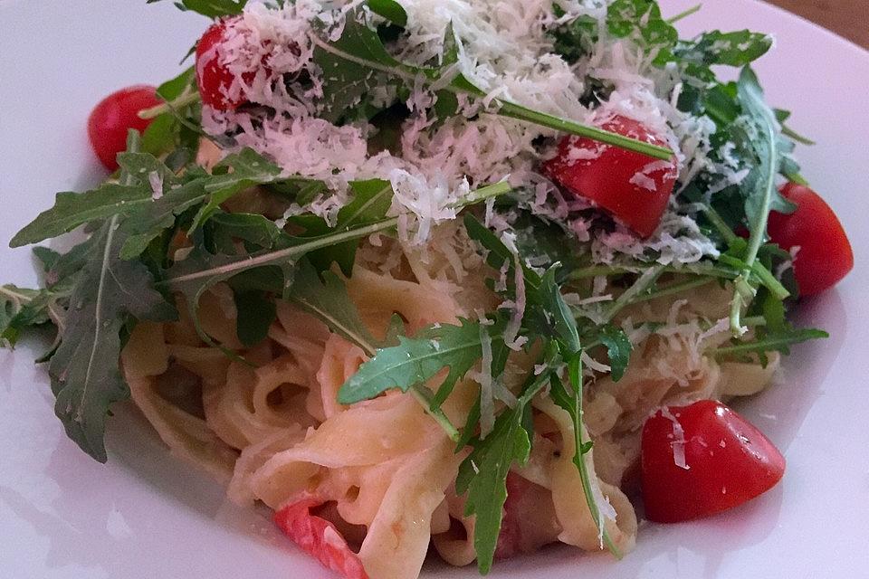 Auf einem Teller ist Tagliatelle in Weißwein-Sahne Soße  zu sehen, drapiert mit Cocktailtomaten und Parmesan.