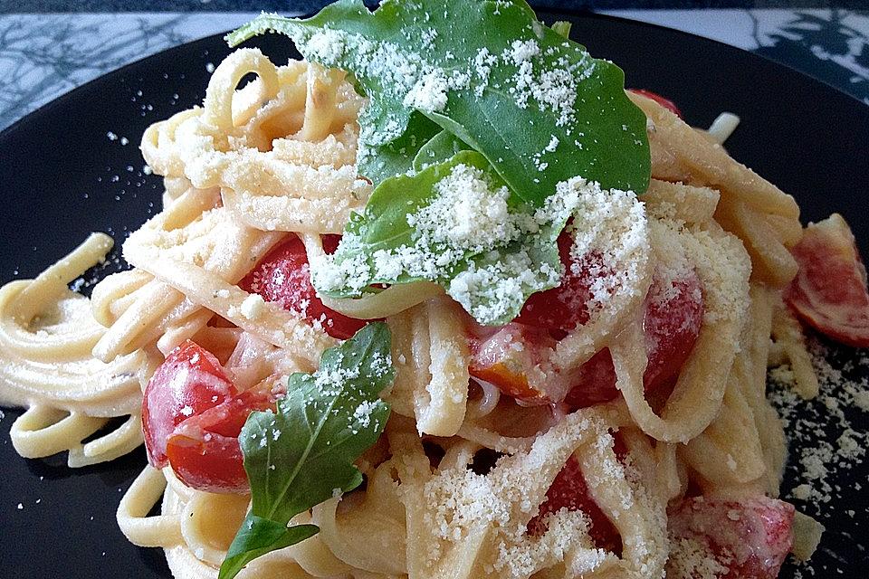 Auf einem Teller ist Tagliatelle in Weißwein-Sahne Soße  zu sehen, drapiert mit Cocktailtomaten und Parmesan.