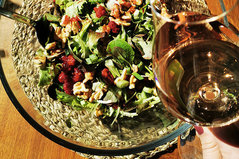 Ein frischer und lecker aussehender frühlingssalat steht vor einem Weinglas gefüllt mir einem leicht schimmernden Rosé